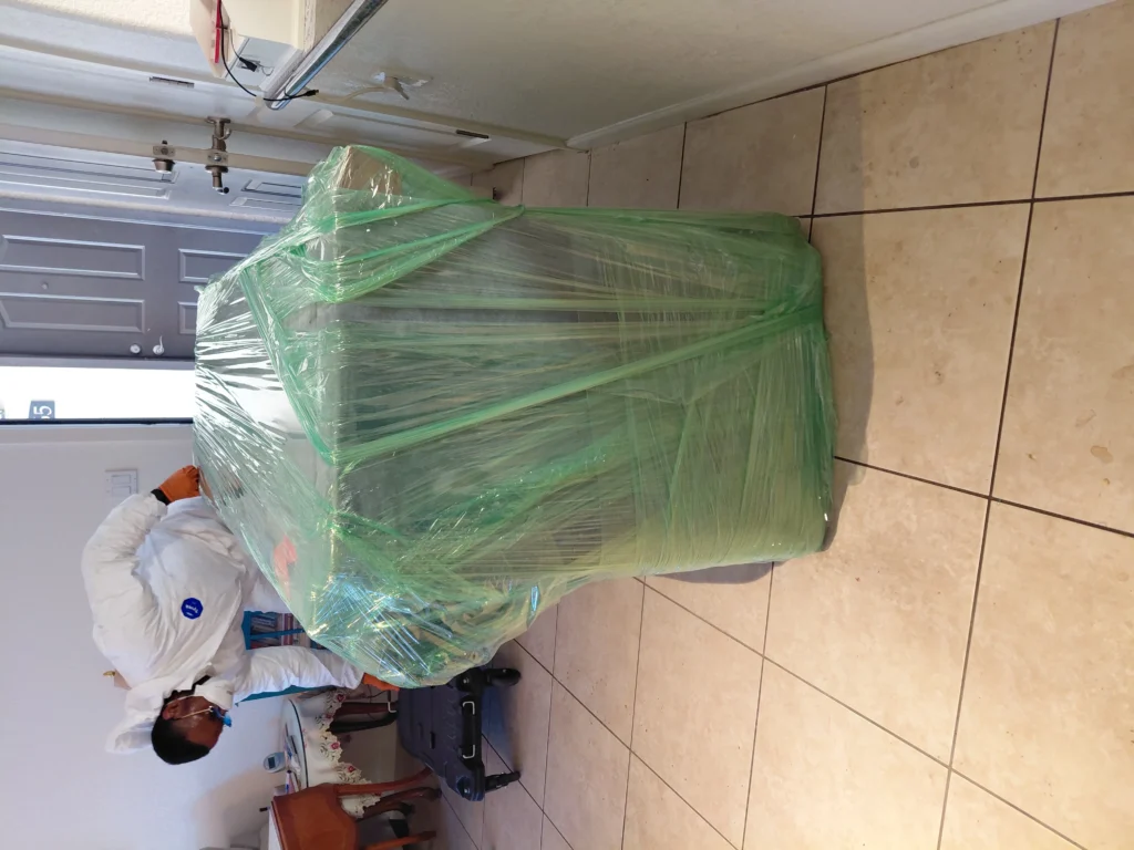 Furniture wrapped in green plastic, with a person preparing to move it.